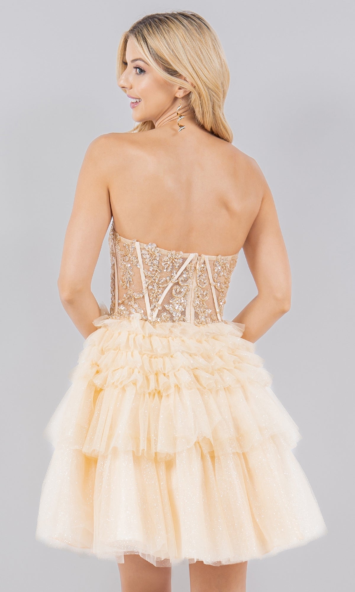 A woman faces backward in the Short Sweetheart Ruffled Homecoming Dress 5133J, a strapless beige lace and tulle A-line semi-formal dress with a tiered ruffled skirt, set against a plain light gray background.